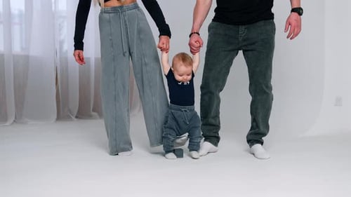 Unrecognized man and woman hold a little baby by the hands. Parents teach their infant son to walk.