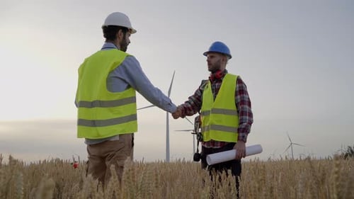 Engineer and Technician Shaking Hands to Implement New Sustainable Project in Field Wind Turbines