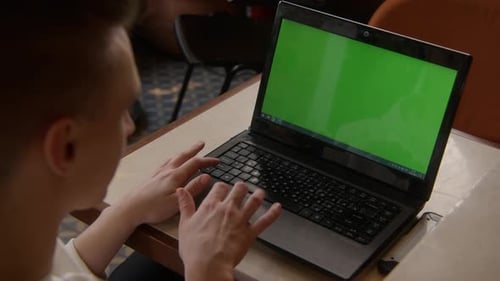 Young man is working at laptop with green screen in cafe. Guy with laptop and green screen in cafe