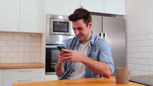 Smiling Man Uses Smartphone in Kitchen