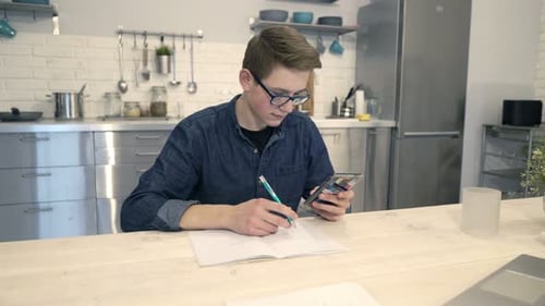 Teen Studying with Phone and Notebook in Kitchen