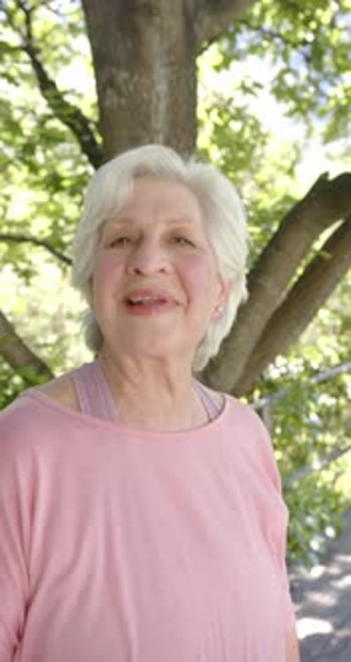 Slow-mo vertical video: joyful elderly white-haired Caucasian woman in sunny nature