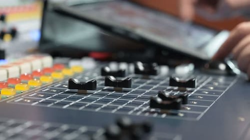 Hand adjusting knob on colorful electric table for mixing tracks in recording studio