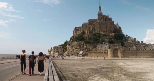 Several Tourists Walking On The Footbridge In Le Mont Saint-Michel In Normandy, France. Wide Shot