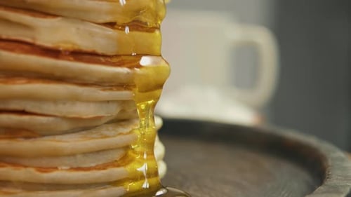 Honey and Maple Syrup Flow Down the Edge of the Pancakes Stacked Appetizingly and Slowly Close Up