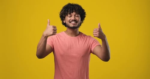 Jeune Indien souriant et heureux montrant le pouce levé comme un geste debout isolé au-dessus d'un studio orange