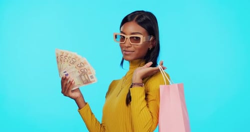 Sales, money and woman with bags, shopping and excited for discount against blue studio background