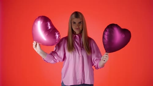 Pretty Blonde Woman Waving Purple Heart Shaped Balloons Against Red Background, Colorful Studio Shot