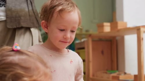 Curious Preschooler Talking While Teacher Arranges Materials in Classroom