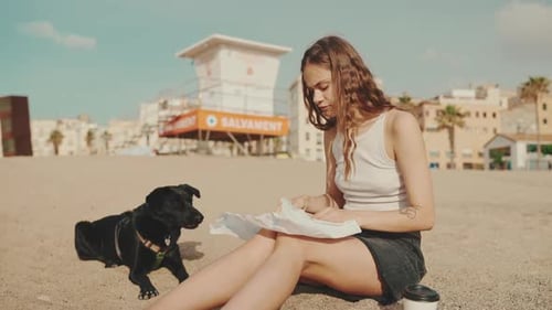 Woman and Black Dog Eating on Beach
