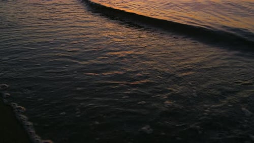 Golden sunrise light reflecting on slow motion ocean waves splashing sand beach