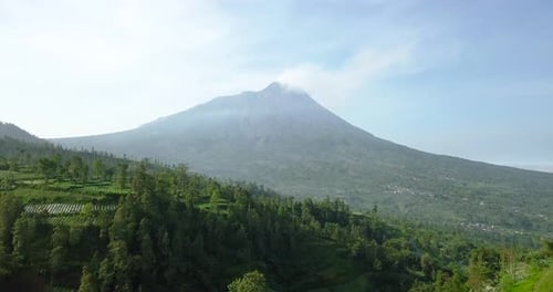 Vulkan Merapi mit ländlicher Aussicht auf Gemüseplantagen und dichten Baumbestand bei leicht nebligem Wetter,
