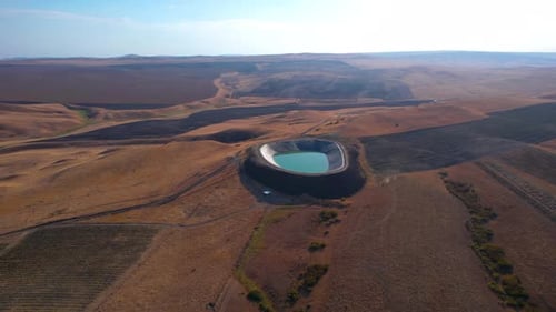 Aerial view of a circular water reservoir in a dry landscape at sunset