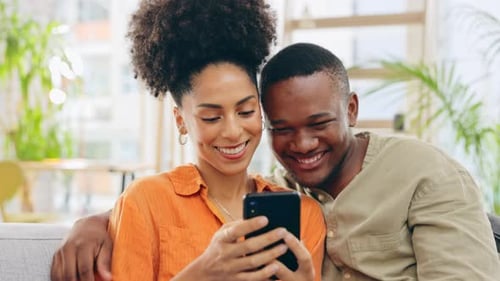 Happy Couple Laughing, Looking at Phone Together Indoors
