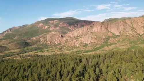 Panning flight over a remote forest area with sunlit rocky cliffs in the distance.