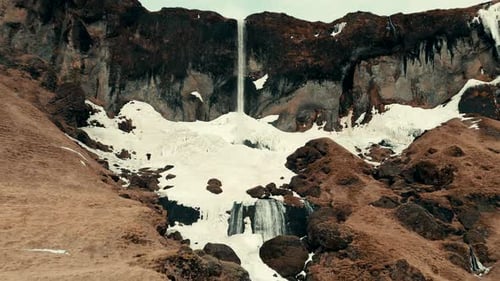 Beautiful Drone Shot Revealing Large Cliff with Glacial Waterfall Falling onto Snowy Rocks, Iceland
