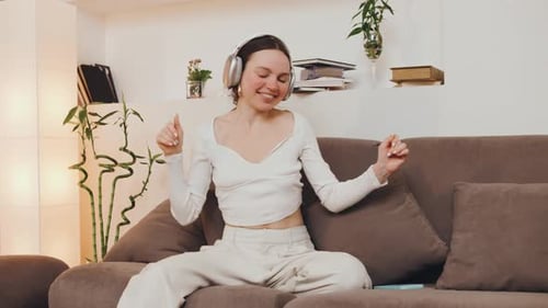Joyful Woman Listening to Music and Dancing on Sofa