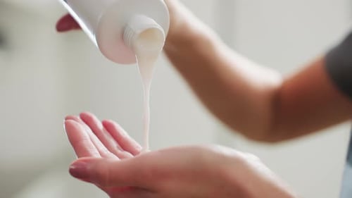 Woman Pours Cream onto Her Hand Indoors