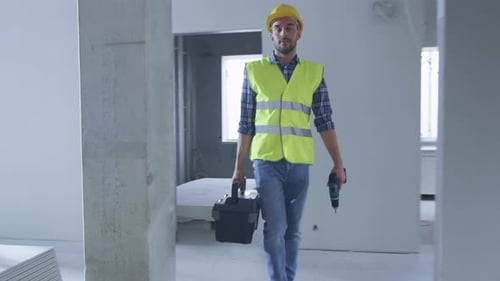Construction Worker Walking inside Building Under Construction and Carrying Toolbox