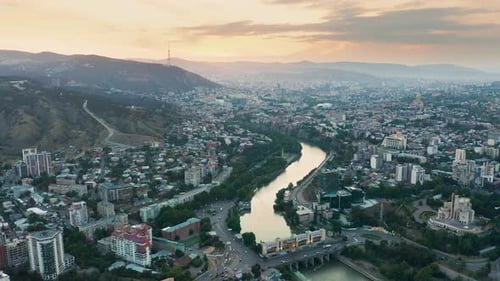 Aerial view of downtown Tbilisi, Georgia at sunset with mountains in the background. Backward motion