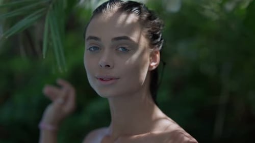 Young woman with wet hair and blue eyes looking at camera with lush green foliage in background