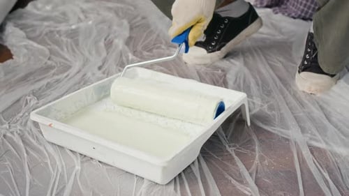 Close-up of Anonymous Man Using Roller Brush to Apply White Paint from Tray