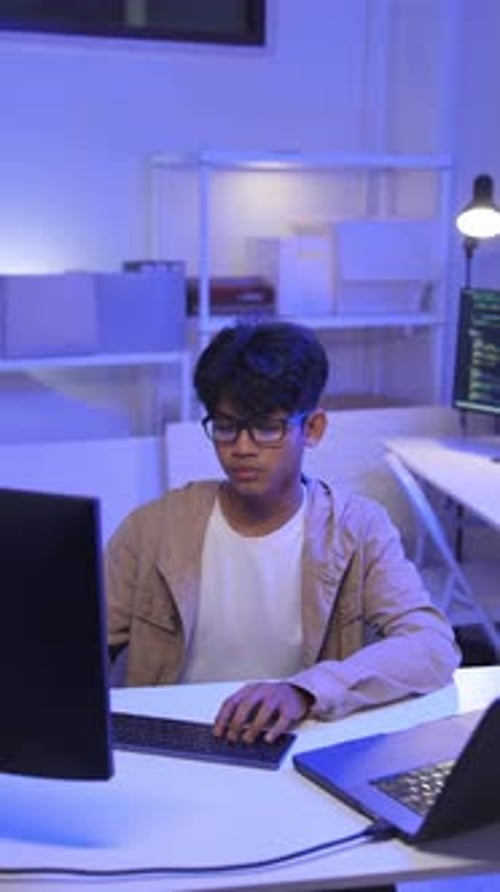 Young Man Typing on Keyboard in a Dark Blue Lit Office