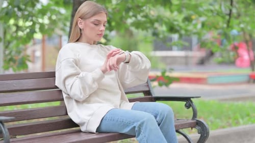 Woman on Bench Checking Smartwatch in City Park