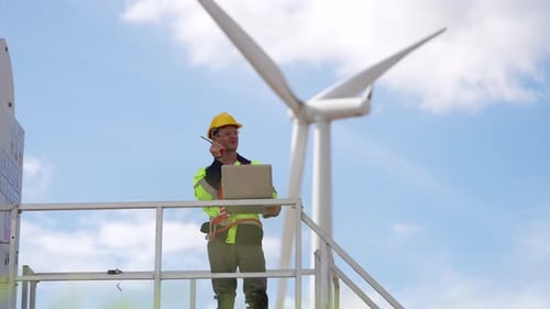 young male engineer working with laptop computer against wind turbine farm