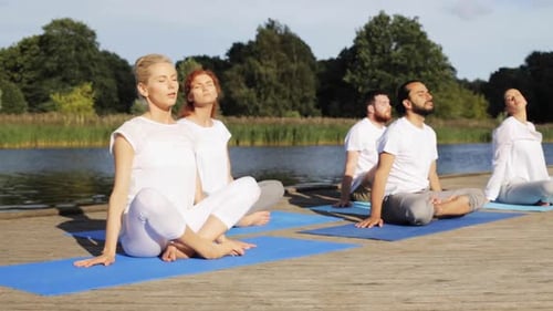 Group practices yoga poses by tranquil lakeside at daytime