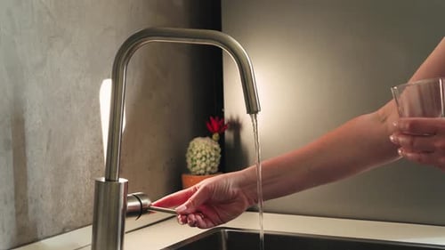 Woman Filling Glass with Water at Kitchen Sink