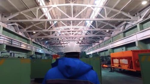 Steel factory worker walking through workshop with industrial equipment