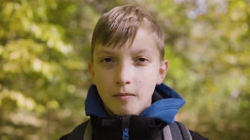 A Cute Young Boy Looks Seriously at the Camera in a Forest Closeup
