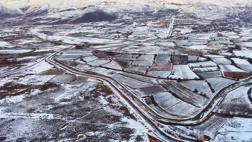 Aerial View of Snowy Farmland and Mountain Valley in Winter