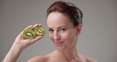 Attractive Woman Holding Kiwi Halves Up to Face
