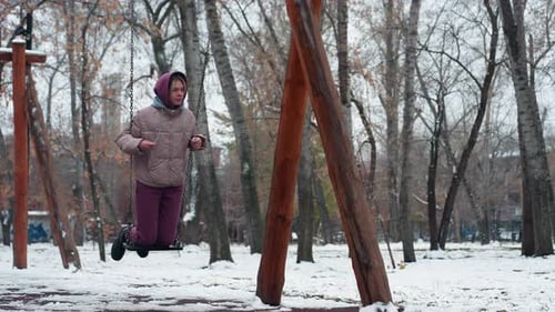 Lady Enjoying Swing Outdoors in Snowy Winter Park with Trees in Background