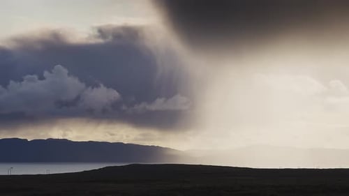 Rain falls from the dark stormy clouds backlit by the sun. Timelapse video.