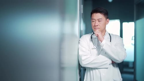 Portrait stressful Asian doctor standing indoors a hospital. Tired pensive thoughtful physician