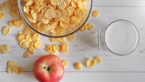 Corn Flakes in Bowl with Glass of Fresh Milk and Appetizing Apple Serving on Wooden Table Top View