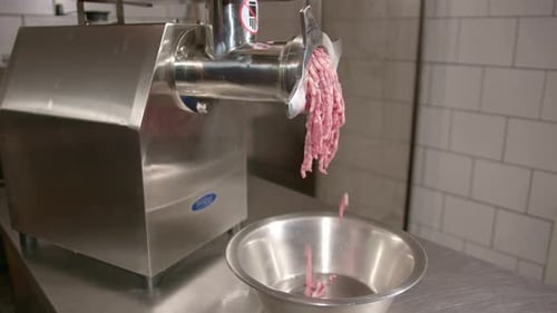 Fresh raw meat being minced in a metal grinding machine, close up
