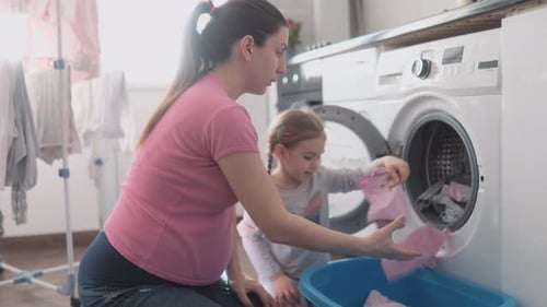 Kleines Mädchen hilft Mama, saubere Wäsche aus der Waschmaschine zu nehmen