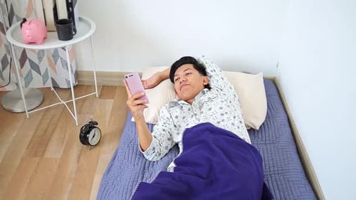 Man Lying on Bed Looking at Cellphone