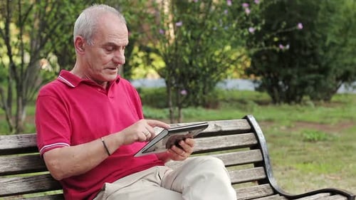 Retired senior man resting and using his tablet at table in park