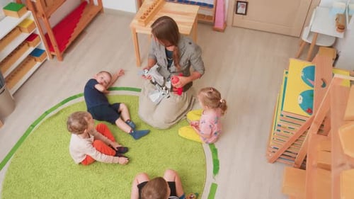 Overhead Daycare Circle As Woman Gathers Toys On Lap
