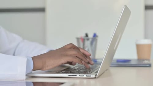 Side View of African Doctor Typing on Laptop