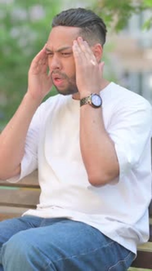 Young Man Sitting Outside Suffering From a Headache