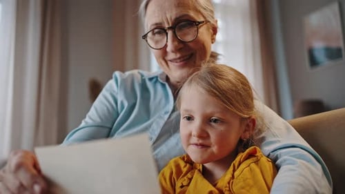 Abuela y nieta mirando álbumes de fotos familiares sonriendo y expresando emociones positivas