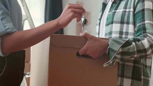 Closeup House Keys in Hand Woman and Man with Box Symbolizing Renting Apartment