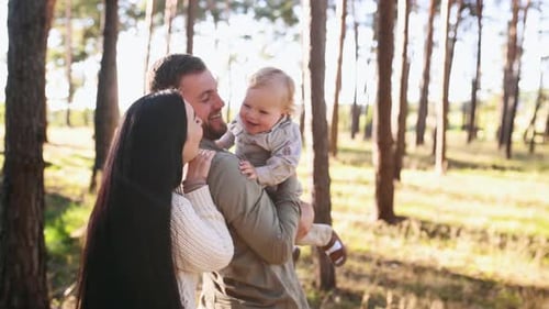 Holding boy in hands and smiling. Family of father, mother and little son is outdoors in the forest