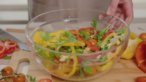 Person pours olive oil on vegetable salad in transparent bowl